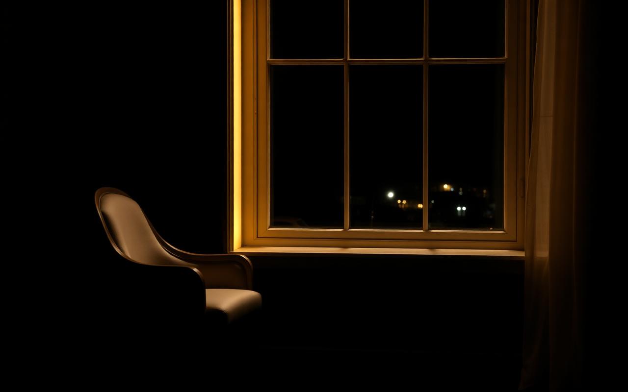 Ventana iluminada de noche junto a una silla vacía